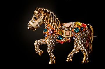 Horse figurine souvenir keychain in gold color ornate with bright pebbles shot on a dark background.