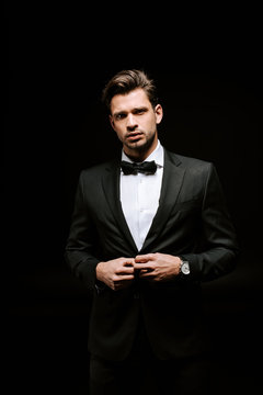 handsome man in suit touching blazer isolated on black