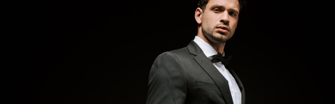 panoramic shot of elegant man in suit looking at camera isolated on black