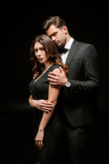 handsome man in suit standing near elegant woman isolated on black