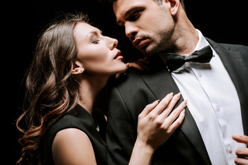 young attractive woman touching handsome man in suit isolated on black