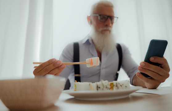 Businessman eating sushi at lunch and looking smartphone.  Entrepreneur inside home studio. Job and modern concept  - Image