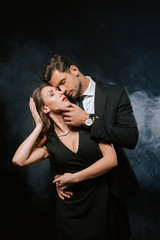 sensual man touching attractive woman in dress on black with smoke