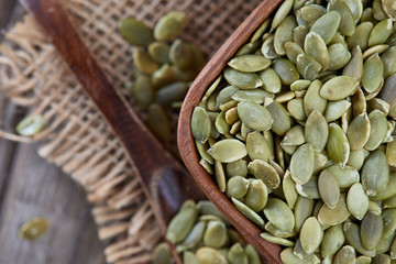 Raw shelled pumpkin seeds in wooden bowl on rustic background