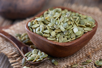 Raw shelled pumpkin seeds in wooden bowl on rustic background