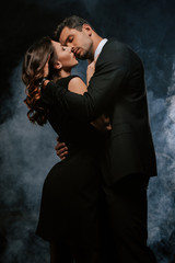 handsome man in suit hugging sensual woman on black with smoke