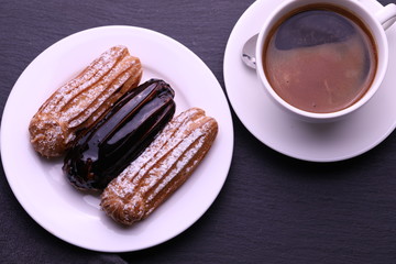Eclair and a cup of coffee on a black wooden table