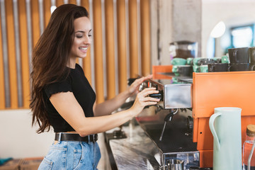 young smiling barista woman working behind the bar, stands near professional coffee machine