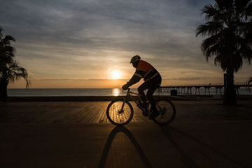 contraluz de hombre en bicicleta paseando por el paseo marítimo