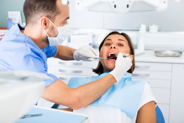 Dentist is treating woman patient which is sitting in dental chair