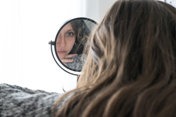 Depressed woman looks herself into mirror with sad face