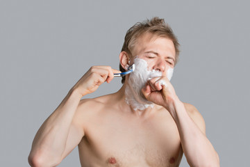 Young shirtless man covering mouth while shaving over colored background