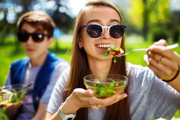 Young couple enjoying lunch outdoor on sunny day. Happy young friends eating natural vegetable salad for lunch. Healthy lifestyle. Concept picnic. Clean eating, vegan food concept.