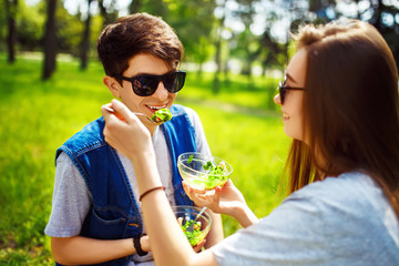 Fototapeta premium Young couple enjoying lunch outdoor on sunny day. Happy young friends eating natural vegetable salad for lunch. Healthy lifestyle. Concept picnic. Clean eating, vegan food concept.