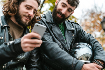 Photo of handsome joyful men smiling and using cellphone