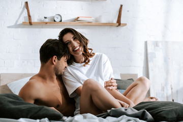 muscular man smiling near happy girlfriend in bedroom