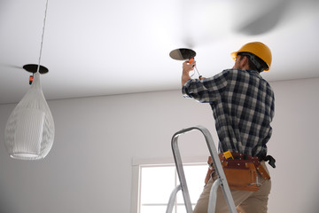 Worker installing lamp on stretch ceiling indoors. Space for text