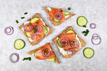 Top view of slices of healthy wholegrain toast bread topped with smoked salmon fish, red onions and spring onions and cucumber on 