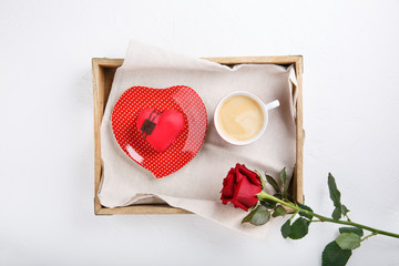 Cup of coffee and heart shaped pink cake on wooden tray. Festive breakfast and red rose on white table. Top view.  Copy space. Happy Valentines day.