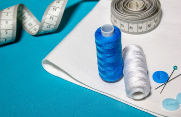 Sewing accessories and fabric on a blue background. Sewing threads, needles, pins, fabric.