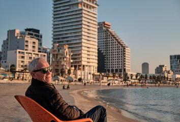 senior old man sitting in a chair realxing in the beach in Tel Aviv - ISRAEL.