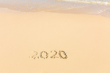 Summer beach holiday 2020 season golden sand - year - decade - new season lettering on the beach with wave and clear blue sea. Numbers 2020 year on the sea shore, message handwritten New Years concept