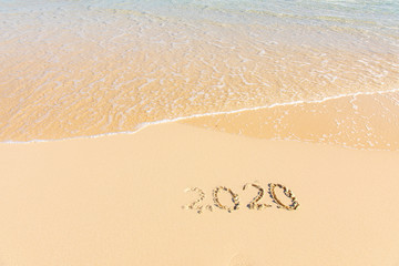 Summer beach holiday 2020 season golden sand - year - decade - new season lettering on the beach with wave and clear blue sea. Numbers 2020 year on the sea shore, message handwritten New Years concept