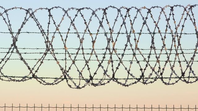 Wrapped barbed wire fence with spikes and sky in the background. Rusted chain link fence guarding high security facility like airport, jail or country boarder