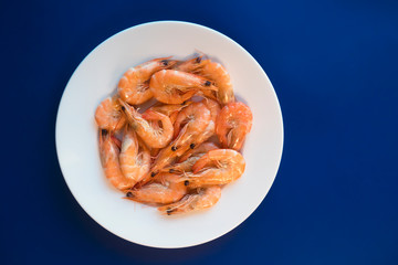 Cooked shripms, fried or boiled seafood, king tiger prawns with green herbs, spices on white plate on dark blue background. Top view. Healthy food. Carbohydrate-free keto protein diet for weight loss