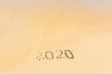Summer beach holiday 2020 season golden sand - year - decade - new season lettering on the beach with wave and clear blue sea. Numbers 2020 year on the sea shore, message handwritten New Years concept