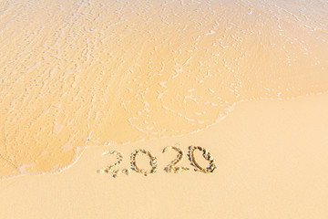 Summer beach holiday 2020 season golden sand - year - decade - new season lettering on the beach with wave and clear blue sea. Numbers 2020 year on the sea shore, message handwritten New Years concept