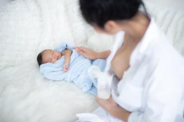 Obraz na płótnie Canvas mother use breast pump to get breast milk and sitting near the sleeping newborn