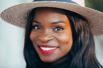Beautiful young black african girl in a hat with a happy smile on the street in the rays of the...
