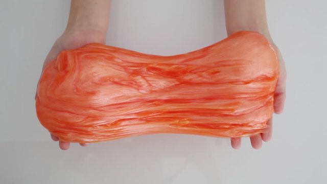 Girl stretching orange slime to the sides. kids hands playing slime toy. Making slime on white. Trendy liquid toy sticks to hands and fingers. Top view