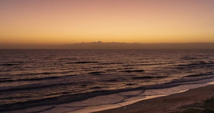 Timelapse clip of a holy grail transition from first light on a beach in Florida into sunrise through clouds. Lights form fishing boats on the horizon.