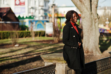 Portrait of a curly haired african woman wearing fashionable black coat and red turtleneck posing...