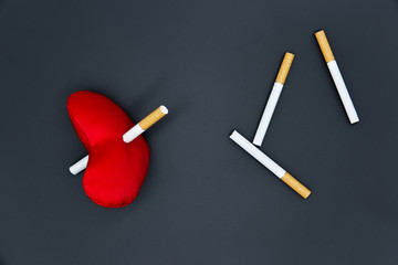 Cigarettes on a black background. A red heart is killed by a cigarette. Diseased heart. The harm of smoking.