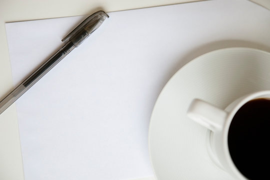 Cropped image of coffee cup with pen on a blank paper