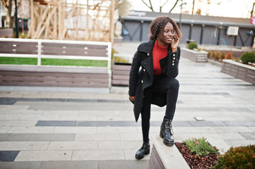 Portrait of a curly haired african woman wearing fashionable black coat and red turtleneck posing outdoor.