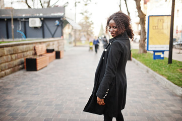 Portrait of a curly haired african woman wearing fashionable black coat and red turtleneck posing...