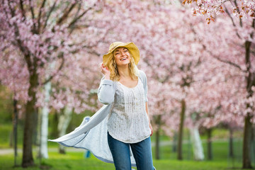 Young woman enjoying the nature in spring. Dancing, running and whirling in beautiful park with cherry trees in bloom. Happiness concept