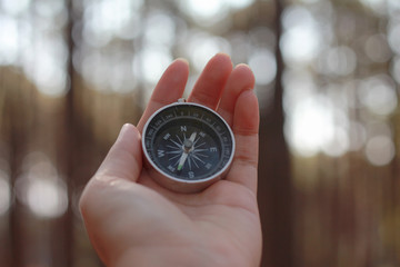 Close up of female hands holding compass against forest.