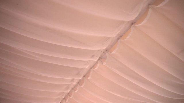 A tent cloth with sagging on white iron tube in light pastel hues. Summer stretch awning on metal construction indoor. Large beige wedding marquee. Pavilion for luxury wedding ceremony.