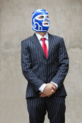Young businessman in pinstripes suit and wrestling mask looking away over gray background