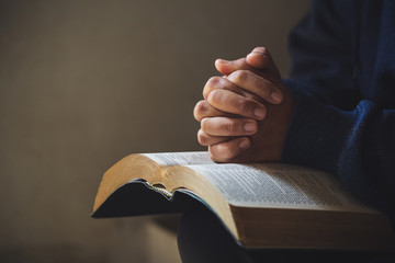 Hands folded in prayer on a Holy Bible in church concept for faith - obrazy, fototapety, plakaty