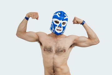 Portrait of a shirtless man in wrestling mask flexing muscles over gray background