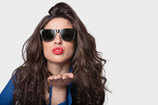 Portrait of a young woman in sunglasses blowing a kiss over gray background