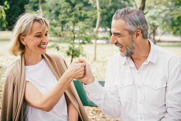 Elderly couple sitting on a bench tease each other having fun and laughing happily together at the public park in the morning. Happy concept of lifestyle in the retirement