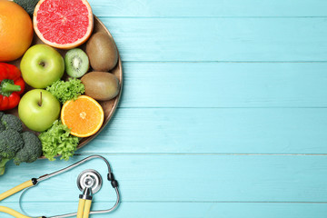 Fruits, vegetables and stethoscope on light blue wooden background, flat lay with space for text....