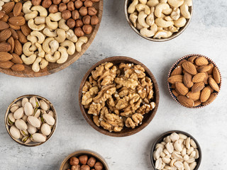 Variety of nuts in wooden plate on grey concrete background. Mixed nuts in wooden bowl. Almond, walnut, peanut, cashew, hazelnut, pistachio. Top view ingredients.